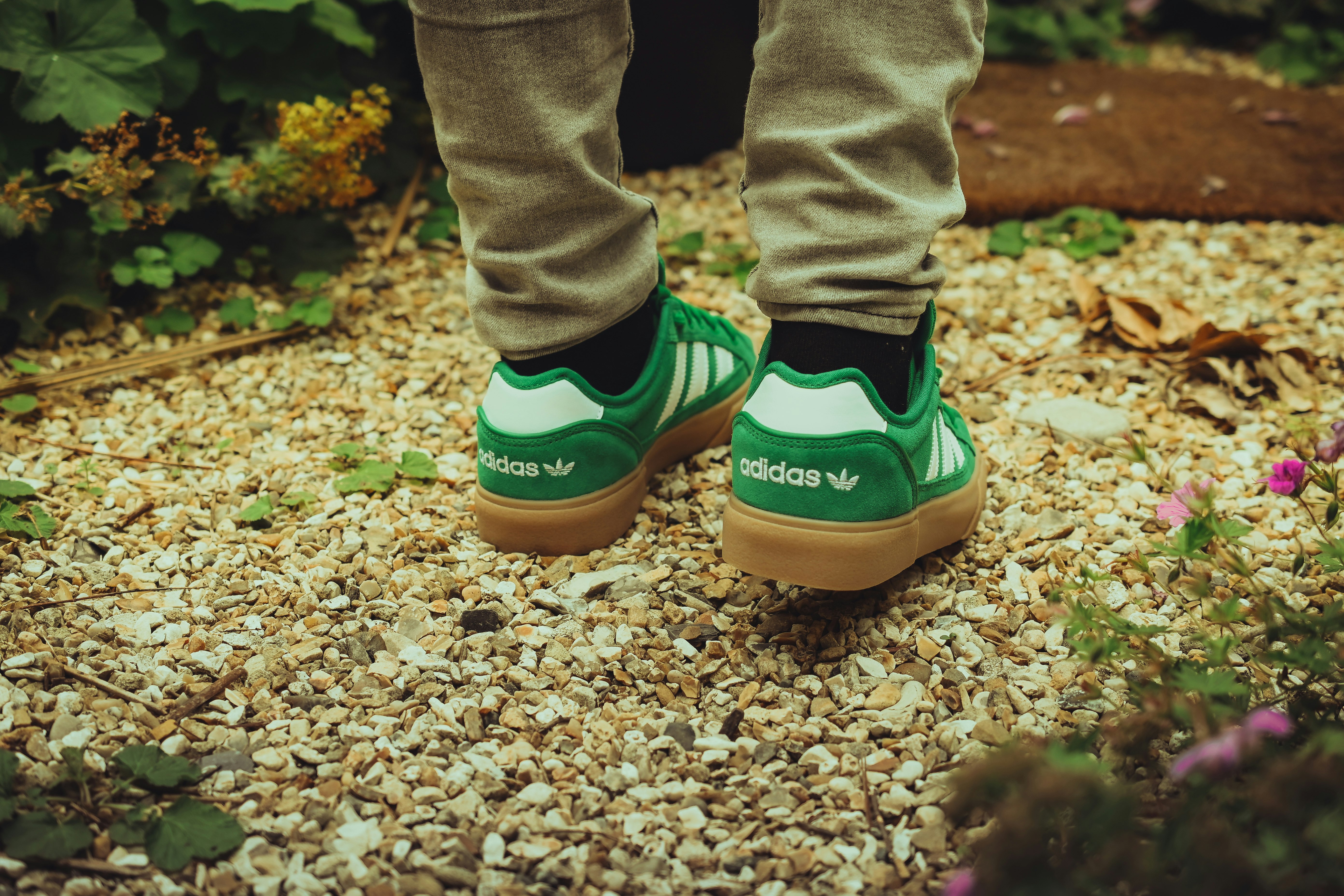 Eco-friendly footwear: a person wearing green adidas shoes standing on gravel
